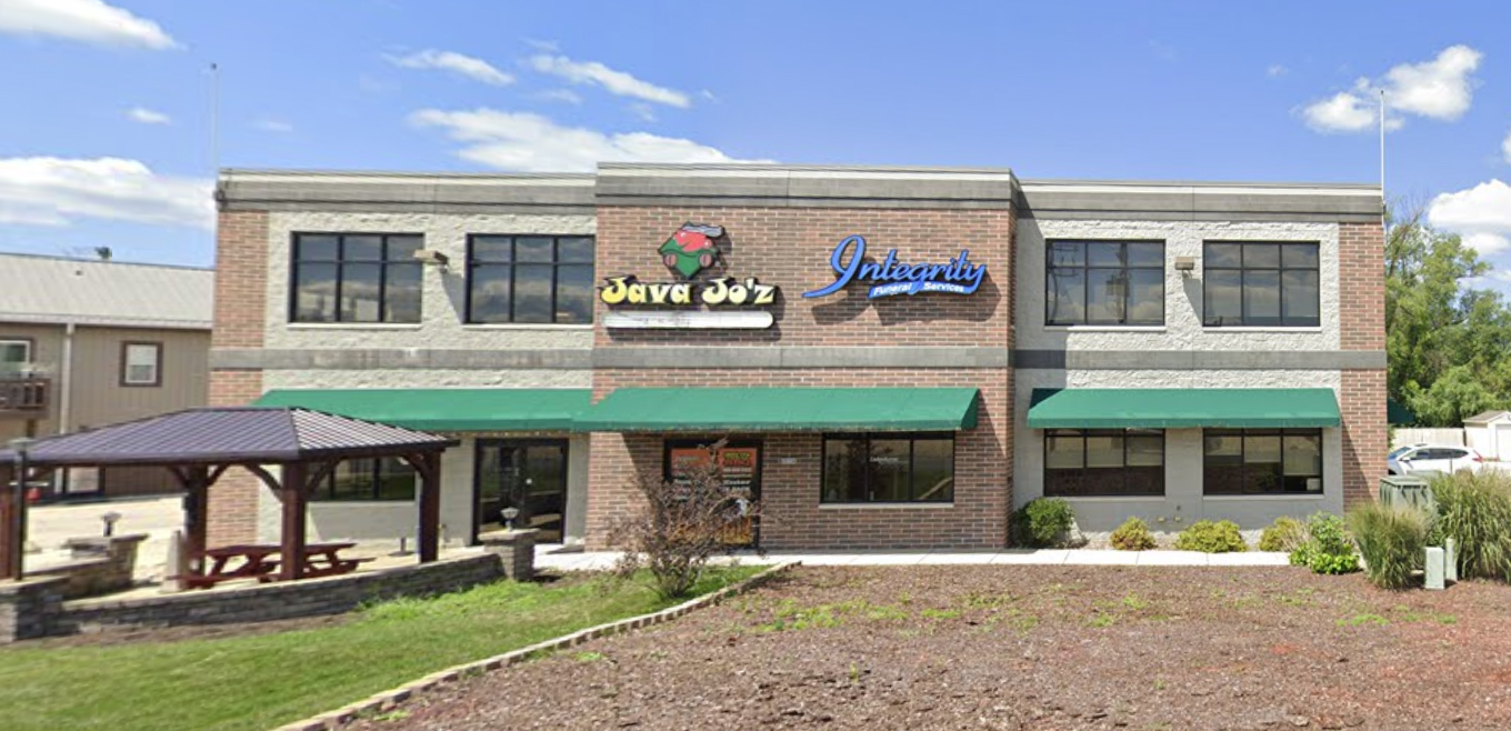 A brown two-story building with green awnings stands independently and displays the signs for several businesses housed within.