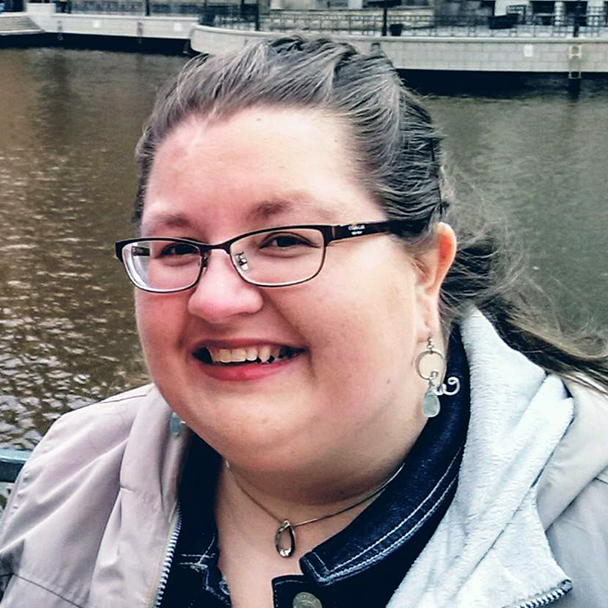 photo of a woman standing in front of a river. Dark hair. Glasses.