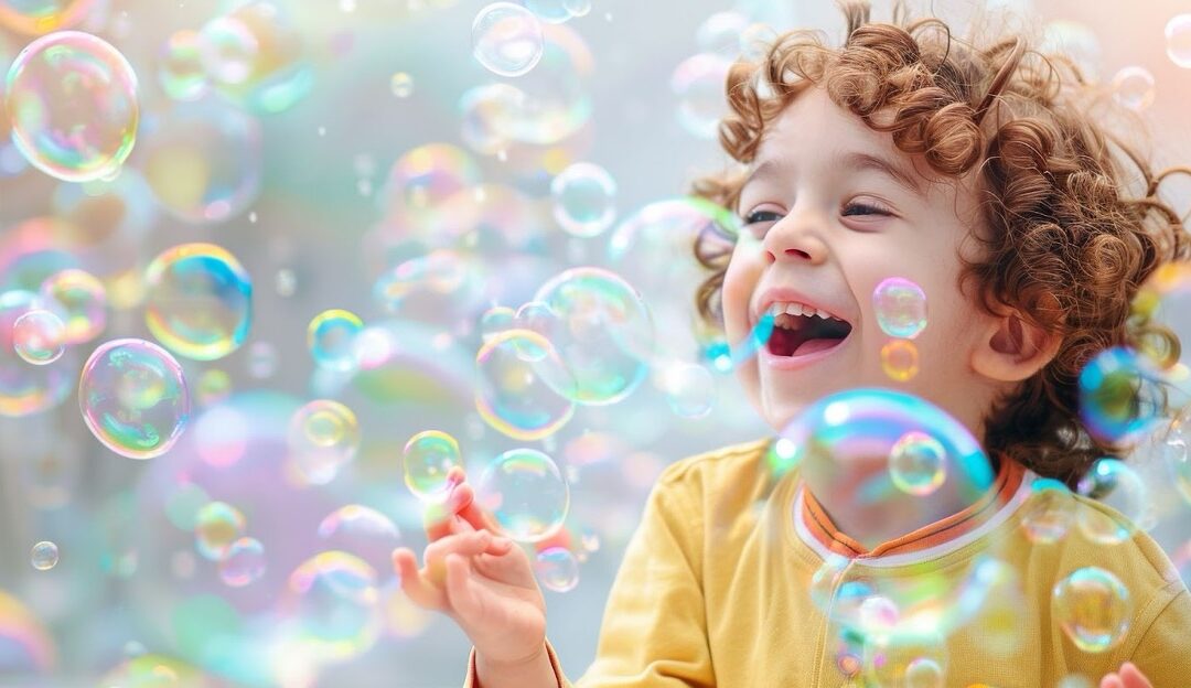 A laughing child with curly brown hair enjoys colorful soap bubbles.