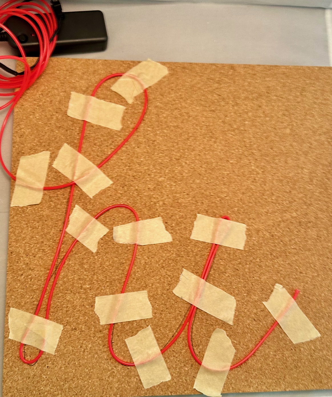 Cork board with red wires taped in loops and a black electronic component.