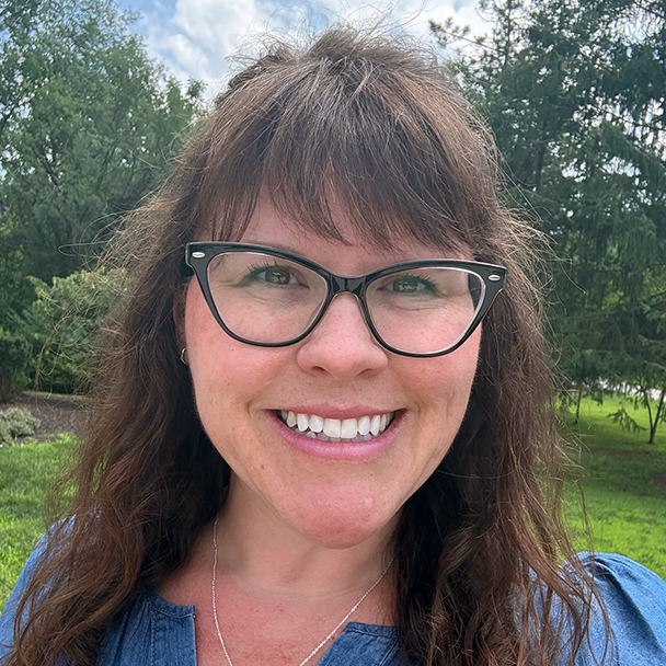 A woman with brown hair and eye glass smiles broadly.