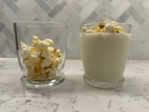 One glass half filled with popcorn and a glass of milk with popcorn on top