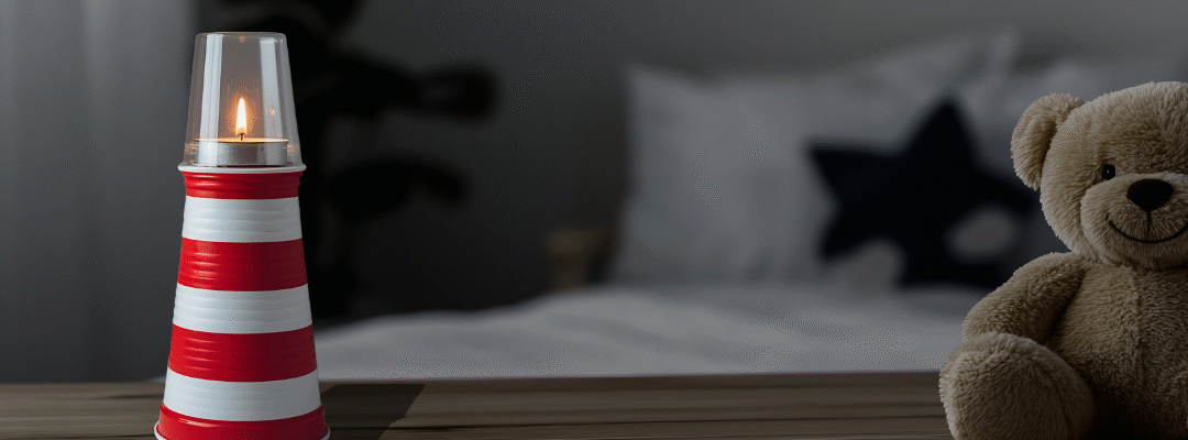 A striped candle holder resembling a lighthouse and a teddy bear on a wooden surface in a cozy bedroom setting.