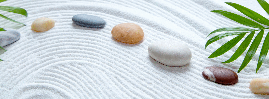 Zen garden with raked sand, colorful pebbles, and green palm leaves.